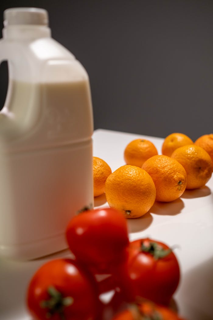gallery-02 A still life composition featuring tomatoes, oranges, and a milk bottle.