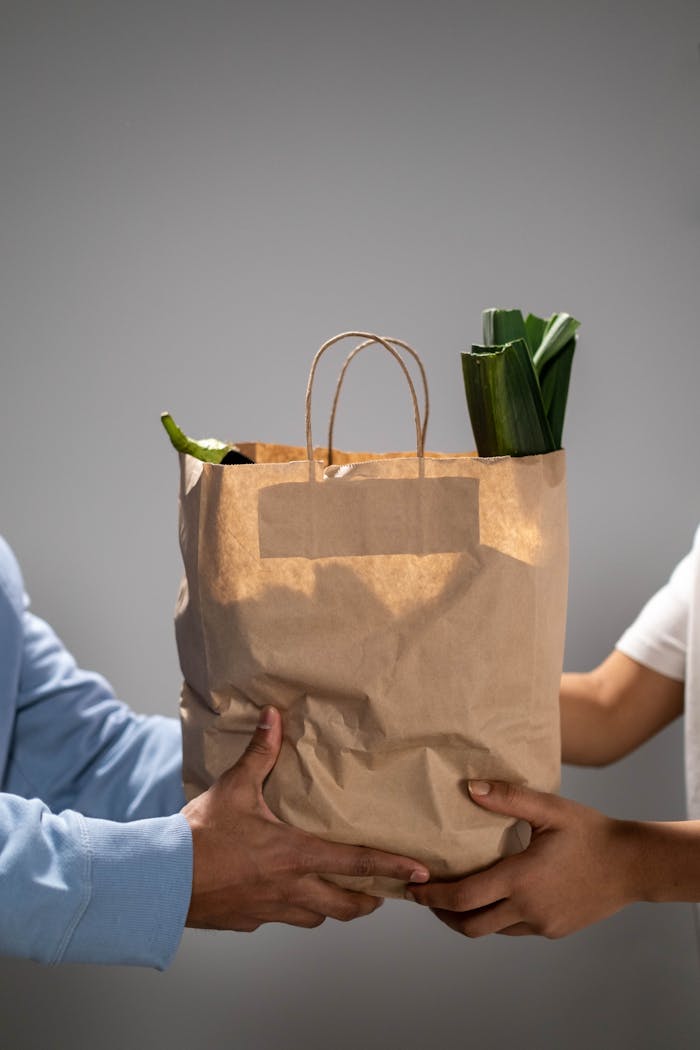 about-img-01 Close-up of hands exchanging a brown paper grocery bag filled with vegetables.